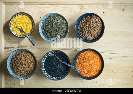 Vari tipi di lenticchie in piccole ciotole su un rustico tavolo di legno Foto Stock