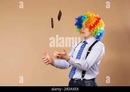 Uomo d'affari che giocola i telefoni cellulari. Primo piano Ritratto di uomo d'affari in parrucca clown. Concetto aziendale Foto Stock