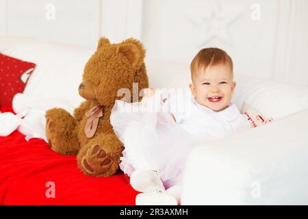 Bella ragazza bambino ridere e divertirsi seduto sul divano all'interno con Natale deco Foto Stock