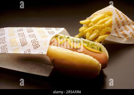Hot dog di Street vendor con senape, sottaceti e un sacchetto di patatine fritte Foto Stock