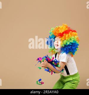 Ragazzo felice clown con grande parrucca colorata. Ragazzino in clown wig che salta e si diverte. Ritratto di Foto Stock