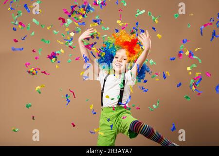 Piccolo ragazzo in clown wig saltando e divertirsi festeggiando il compleanno. Il ritratto di un bambino lancia un Foto Stock