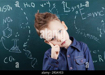 Genius boy vicino a una lavagna con formule. Divertente ritratto ragazzo allievo intelligente sullo sfondo del tabellone della scuola Foto Stock