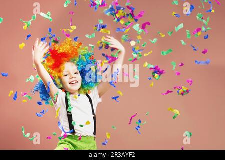 Piccolo ragazzo in clown wig saltando e divertirsi festeggiando il compleanno. Il ritratto di un bambino lancia un Foto Stock