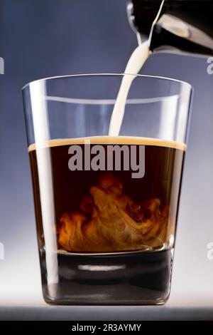 Il latte viene versato in un bicchiere con espresso Foto Stock