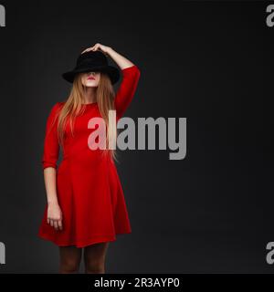 Una bella ragazza vestita di rosso che tiene il suo cappello. Ragazza che tiene cappello a faccia Foto Stock