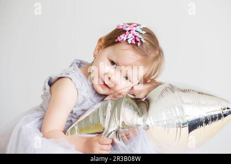 Ritratto di una bella bambina in elegante abito grigio di fronte ad uno sfondo bianco. Piccolo principe Foto Stock