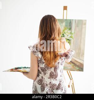 Donna pittura su una tela su sfondo bianco. Vista posteriore. Foto Stock