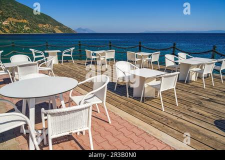 Bar vuoto con sedie e tavoli sul lungomare sotto un cielo blu d'estate. Foto Stock