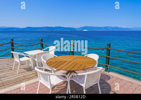 Bar vuoto con sedie e tavoli sul lungomare sotto un cielo blu d'estate. Foto Stock