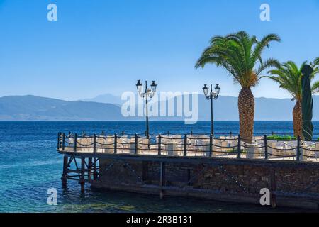 Bar vuoto con sedie e tavoli sul lungomare sotto un cielo blu d'estate. Foto Stock