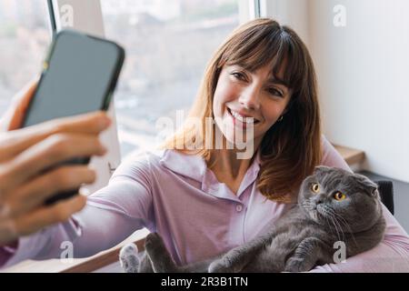 Donna felice che prende selfie con gatto attraverso smartphone Foto Stock