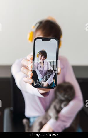 Donna felice con cuffie e gatto che prende selfie attraverso lo smartphone Foto Stock