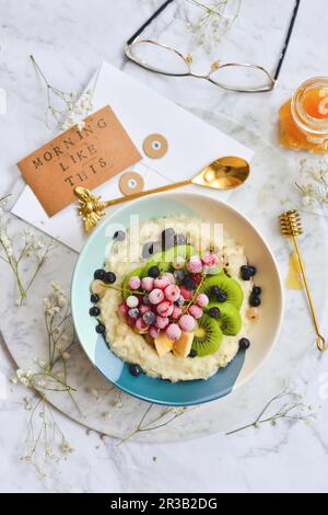 Farina d'avena in una ciotola con frutta surgelata di stagione ribes bacche kiwi Foto Stock