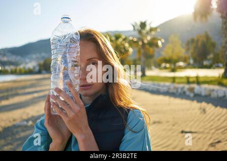 Volontario che tiene una bottiglia di plastica vuota vicino al viso in spiaggia Foto Stock