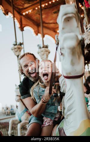 Padre e figlia che si stacca fuori lingua godendosi un giro in giostra al parco divertimenti Foto Stock