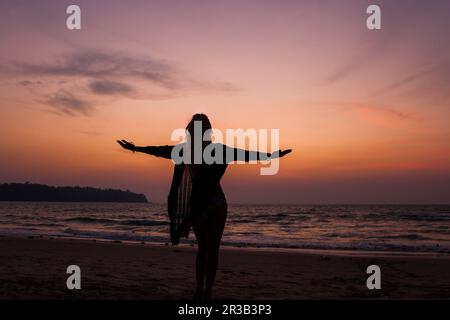 Silhouette di donna in piedi con le braccia in piedi in spiaggia Foto Stock