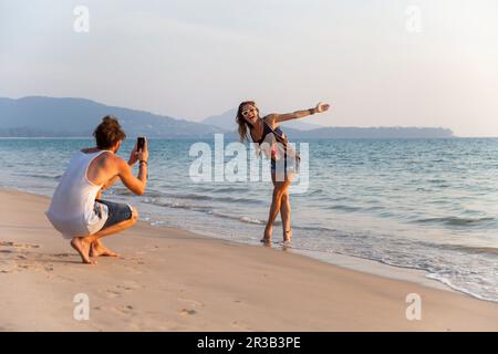 Uomo fotografando ragazza godendosi vicino alla riva alla spiaggia Foto Stock