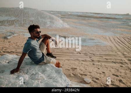 Giovane uomo seduto sulla roccia nel deserto Foto Stock