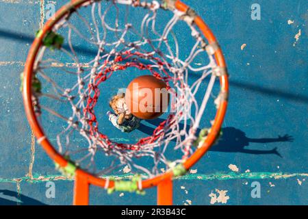 Figlio che lancia il basket in piedi sotto il cerchio Foto Stock