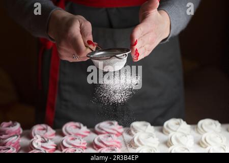 Il processo di produzione di marshmallow. Primo piano le mani dello chef con setaccio in metallo cosparso di zephyr Foto Stock