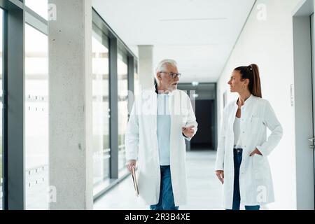 Medico senior che discute con un collega che cammina nel corridoio dell'ospedale Foto Stock