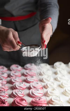 Il processo di produzione di marshmallow. Primo piano le mani dello chef con setaccio in metallo cosparso di zephyr Foto Stock