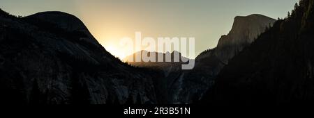 Silhouettes di North Dome e Half Dome come il sole sorge sopra il crinale dietro di loro in Yosemite Foto Stock