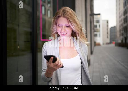 Donna sorridente che tiene il telefono cellulare sul marciapiede Foto Stock