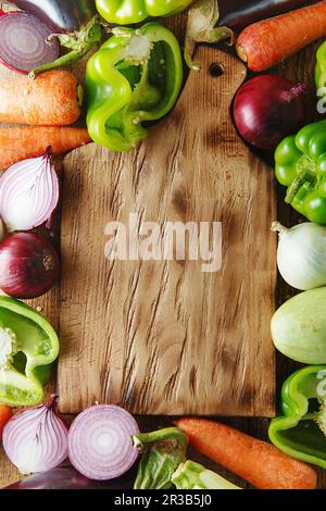 Verdure fresche e ingredienti per cucinare intorno al tagliere d'annata su sfondo rustico, top Foto Stock