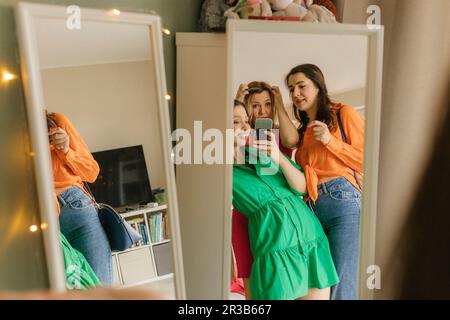 Donna che prende selfie specchio con gli amici che vanno per la festa a casa Foto Stock