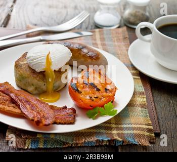 Colazione inglese completa, con pancetta croccante, uova in camicia, pomodoro alla griglia, salsiccia e hash brown Foto Stock