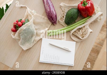 Lista di shopping da verdure fresche in sacchetti riutilizzabili sul tavolo a casa Foto Stock