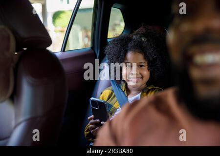 Ragazza sorridente che tiene lo smartphone seduto in auto Foto Stock
