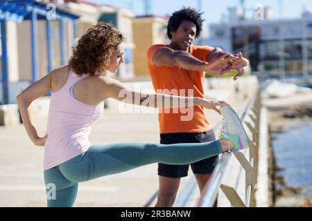 Coppia che si allunga e si esercita sul molo nella zona costiera Foto Stock