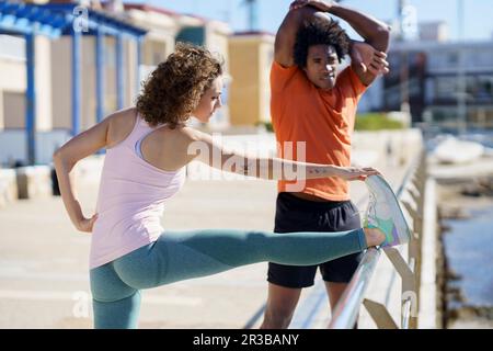 Coppia che si allunga e si esercita sul molo nella zona costiera Foto Stock