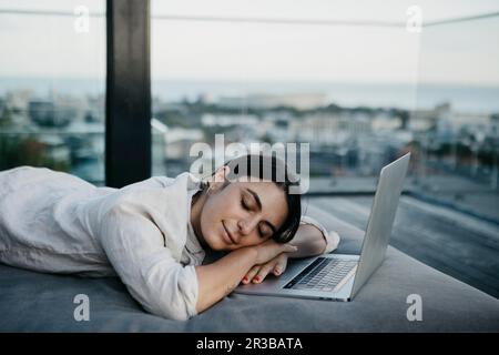 Freelance stanco che riposa sul divano con un computer portatile Foto Stock