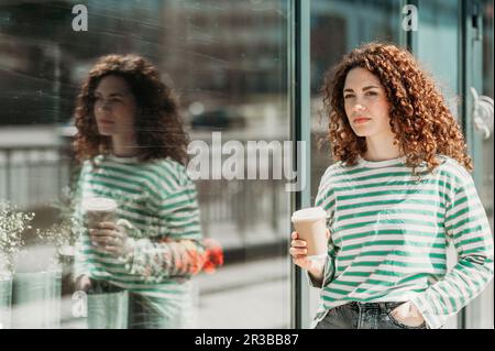 Donna premurosa con mano in tasca che tiene una tazza da caffè usa e getta Foto Stock