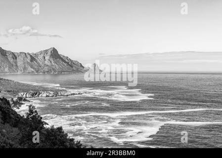 Vista da Clarence Drive vicino a Gordons Bay nella provincia di Western Cape. Rooiels è visibile attraverso la baia. Monocromatico Foto Stock