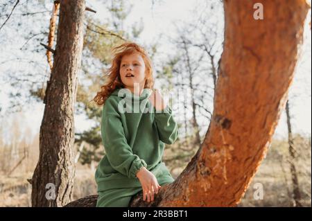 Ragazza Redhead seduta su ramo di albero nella foresta Foto Stock