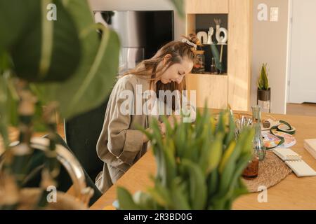 Giovane donna sorridente che fa opere d'arte a casa Foto Stock