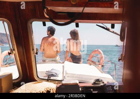 Uomo e donna seduti sul prua della nave, visti attraverso il parabrezza Foto Stock