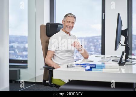 Ritratto di medico sorridente seduto alla scrivania in pratica medica Foto Stock
