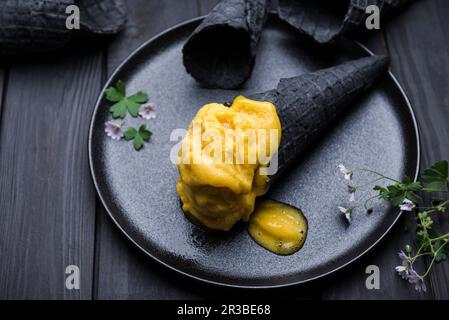 Sorbetto al mango vegano in un cono di cialda nero Foto Stock