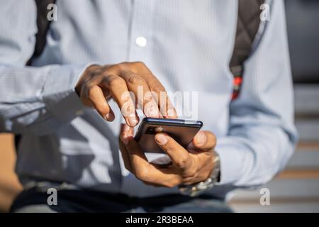 Dettaglio delle mani di un Latino con un telefono cellulare visto dalla parte anteriore. Foto Stock