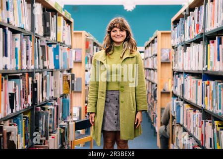 Giovane donna sorridente in piedi tra libreria Foto Stock