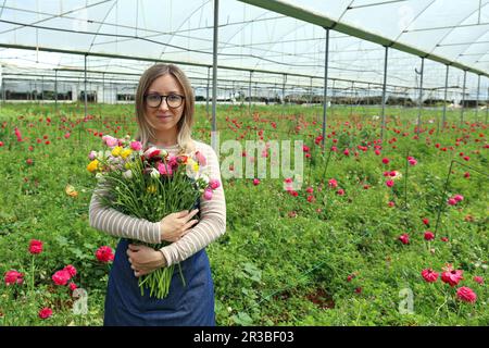 Sorridente contadino che tiene mazzo di fiori in piedi in serra Foto Stock