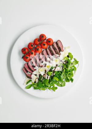 Tagliata di bistecca con pomodori ciliegini, rucola e parmigiano Foto Stock