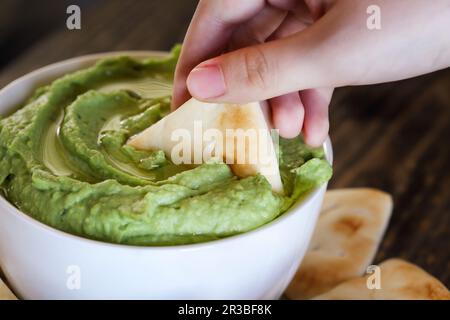 Mano della donna che immerga il pane pita nell'hummus vegano dell'avocado Foto Stock