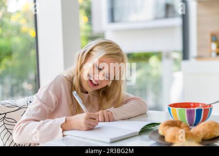 Ragazza bionda sorridente che fa i compiti a casa Foto Stock